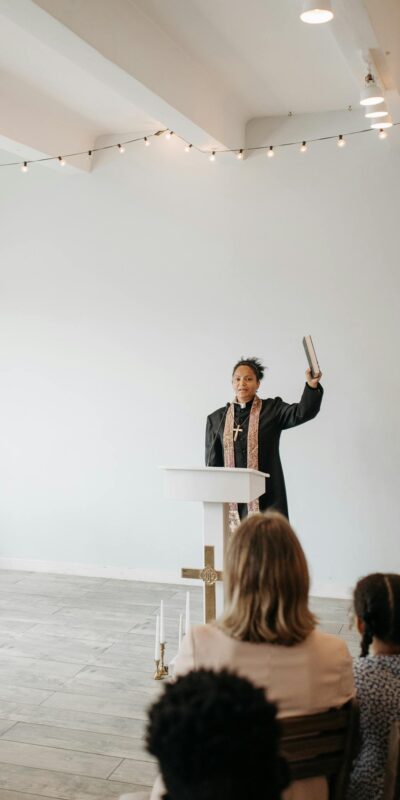 A female pastor delivering a sermon to a small congregation in a minimalist church interior.