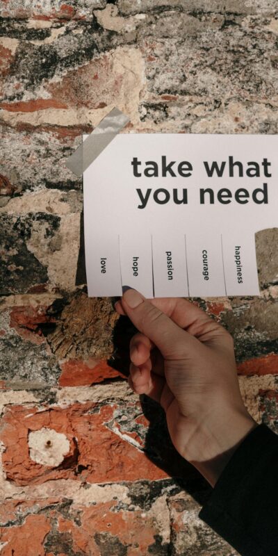 A hand holding a paper note taped on a brick wall with motivational words to pick from.