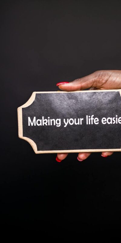 A hand holding a sign with the quote 'Making your life easier!' against a black background.