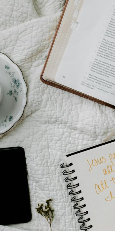 Flat lay of Bible study with coffee, notebook, and phone on a quilted blanket.